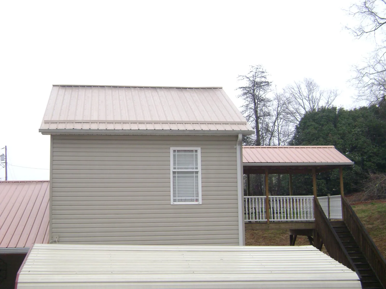 Tan metal roofs on a two story addition and attached porch, from a Roof Replacement job in Martin
